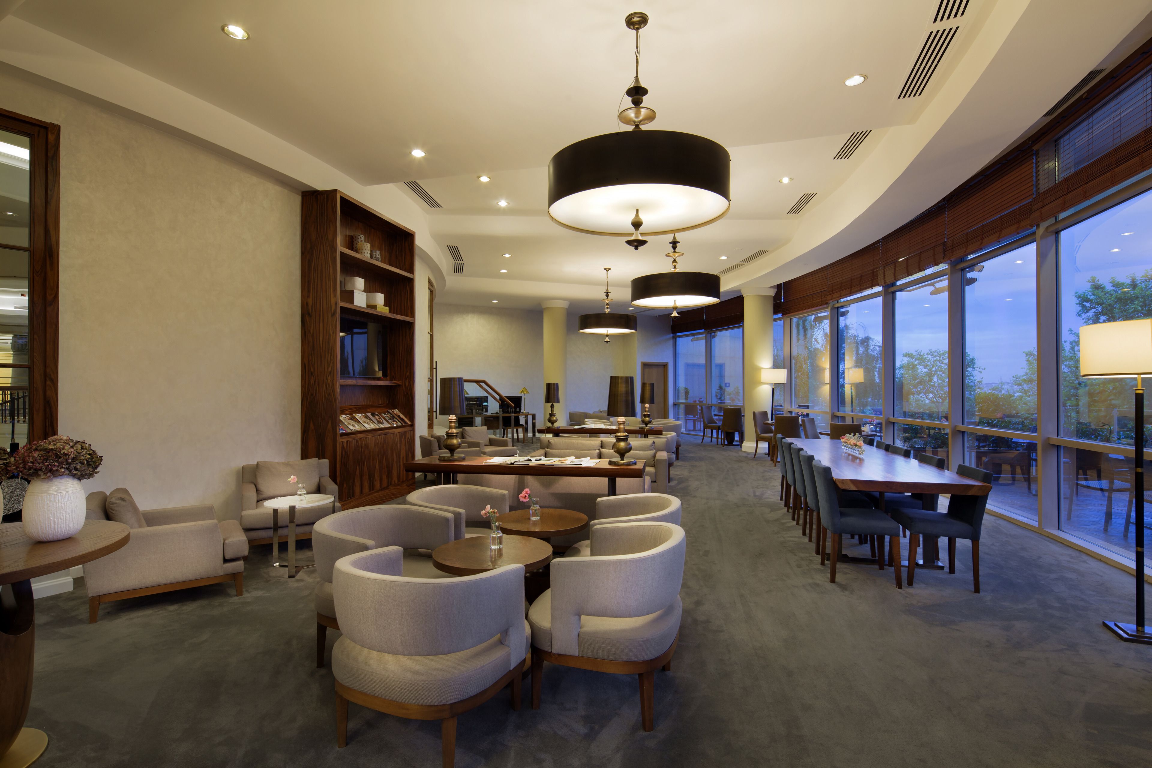 A spacious hotel lobby with a large seating area, a reception desk, and large windows offering a view of the outdoors.