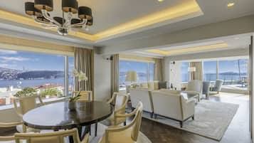 A spacious living area with a dining table, comfortable seating, and large windows offering a view of the city and water.