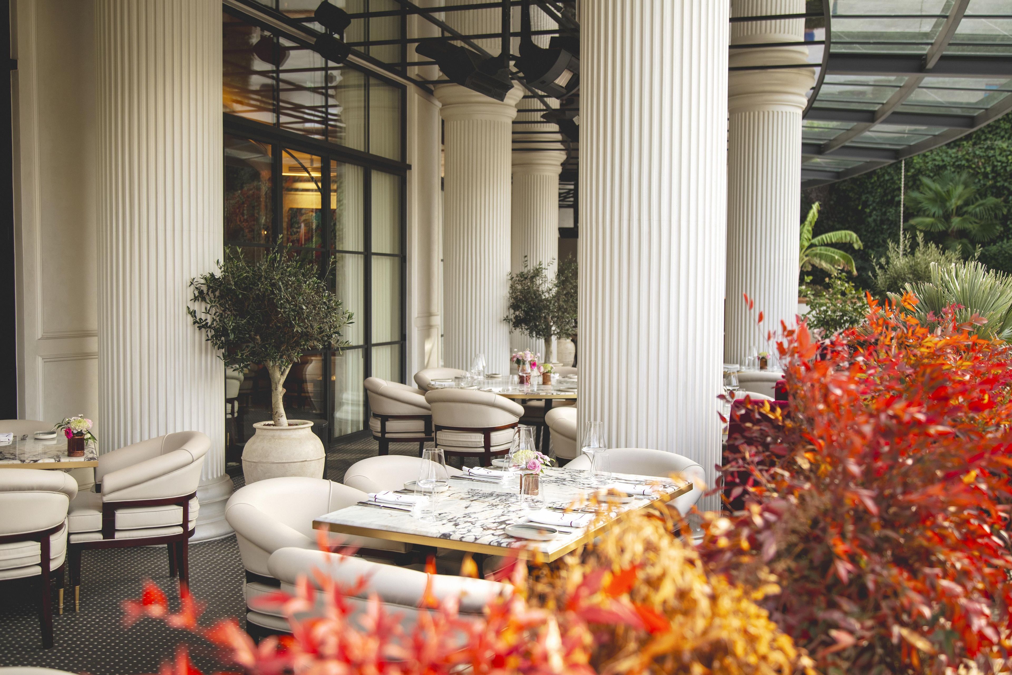 An outdoor dining area with white columns, leather chairs, and tables set for dining.
