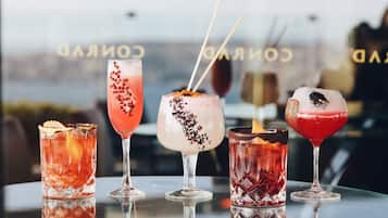 Vier Cocktails auf einer spiegelnden Oberfläche, im Hintergrund verschwommen der Schriftzug 'CORAL'.