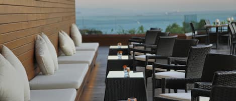 A terrace with outdoor seating and tables, overlooking a body of water.