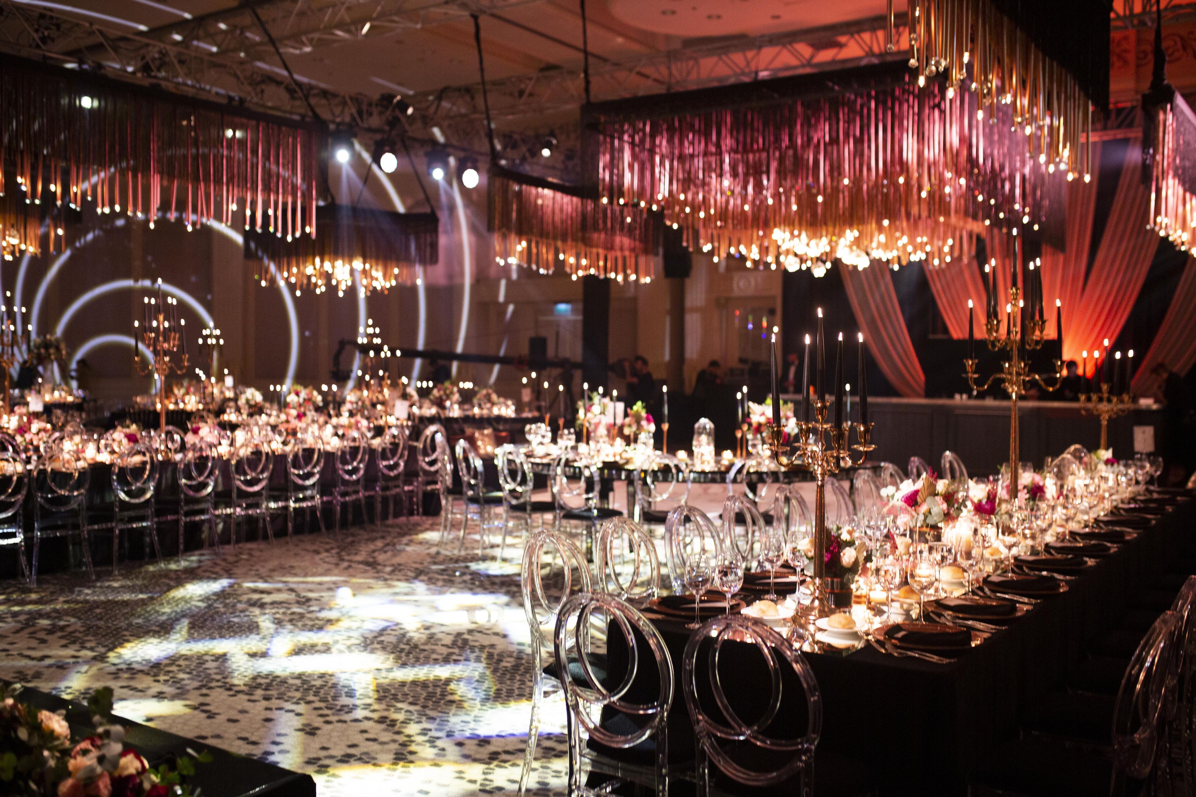 A banquet hall with long tables set for a formal event, featuring chandeliers and draped curtains.