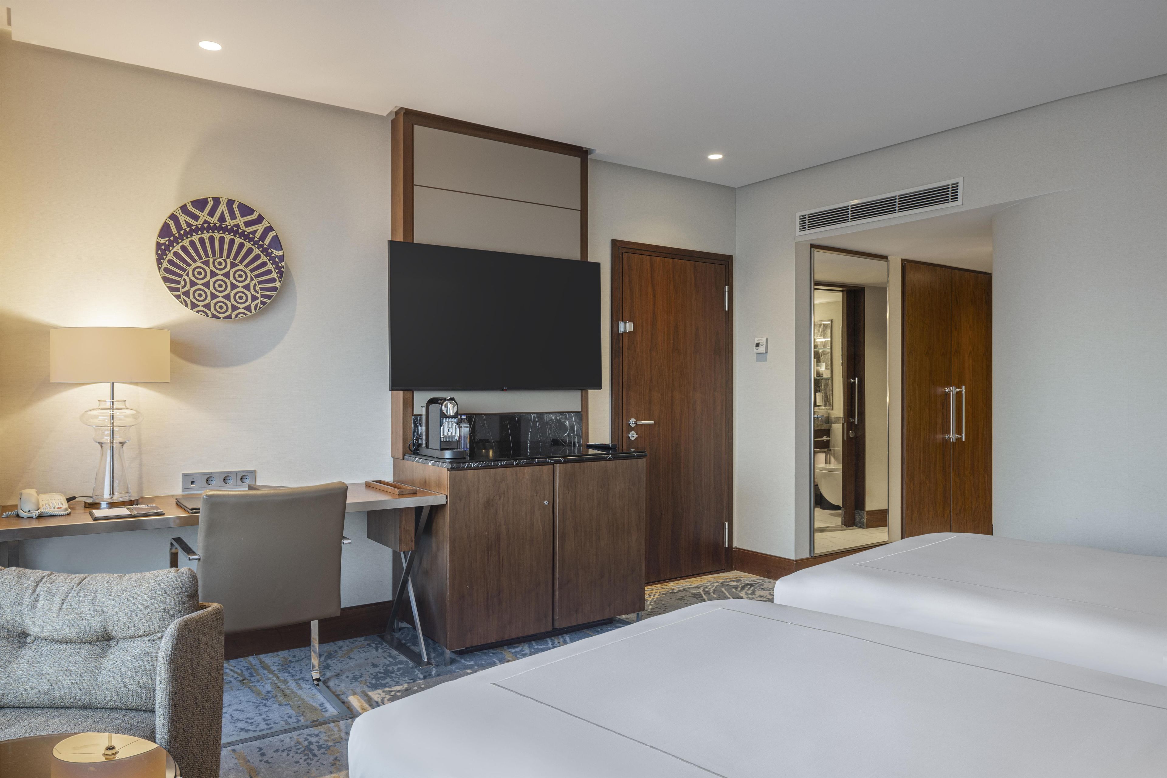 Une chambre d’hôtel comprenant un lit, un bureau avec une chaise, une machine à café, une télévision et une armoire.