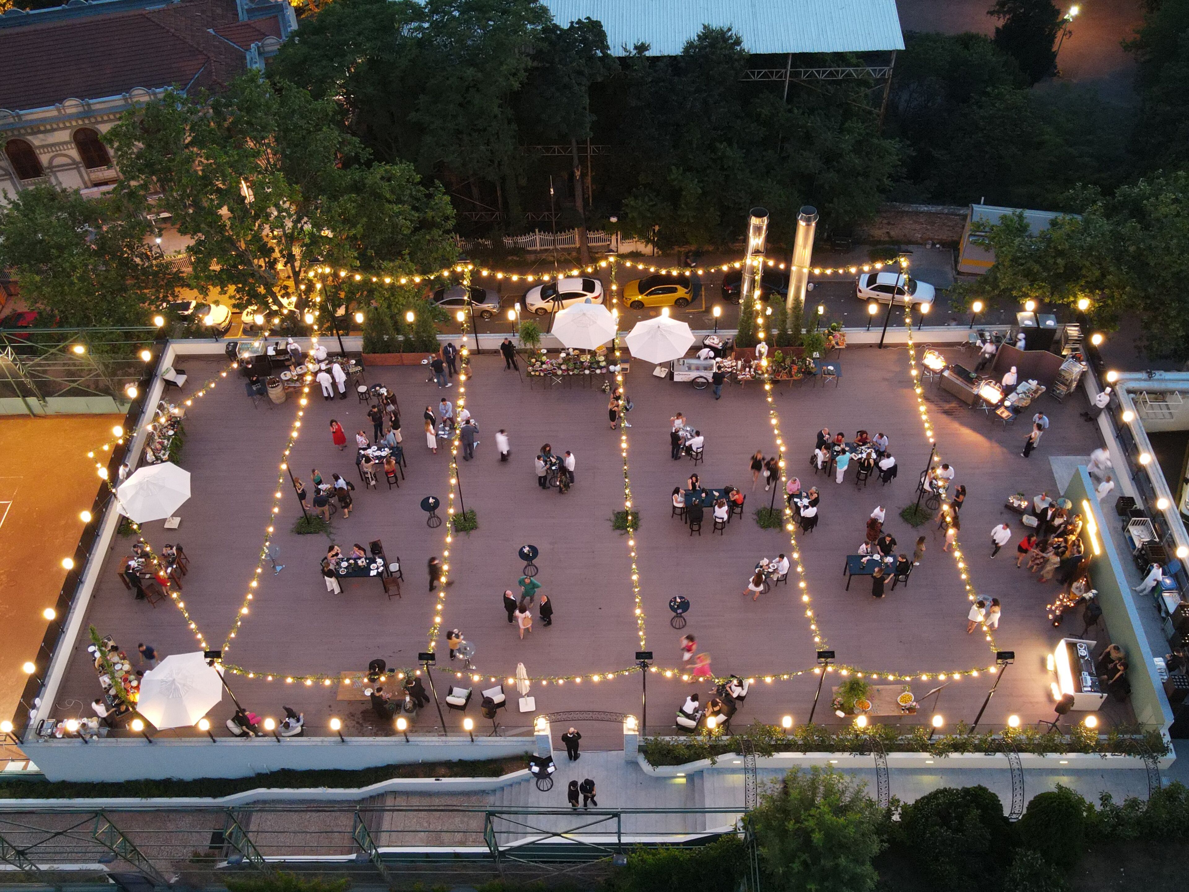 An outdoor dining area with tables and chairs, surrounded by string lights and umbrellas.