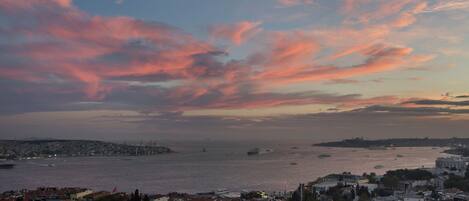 A coastal cityscape with a view of the sea and a sunset sky.