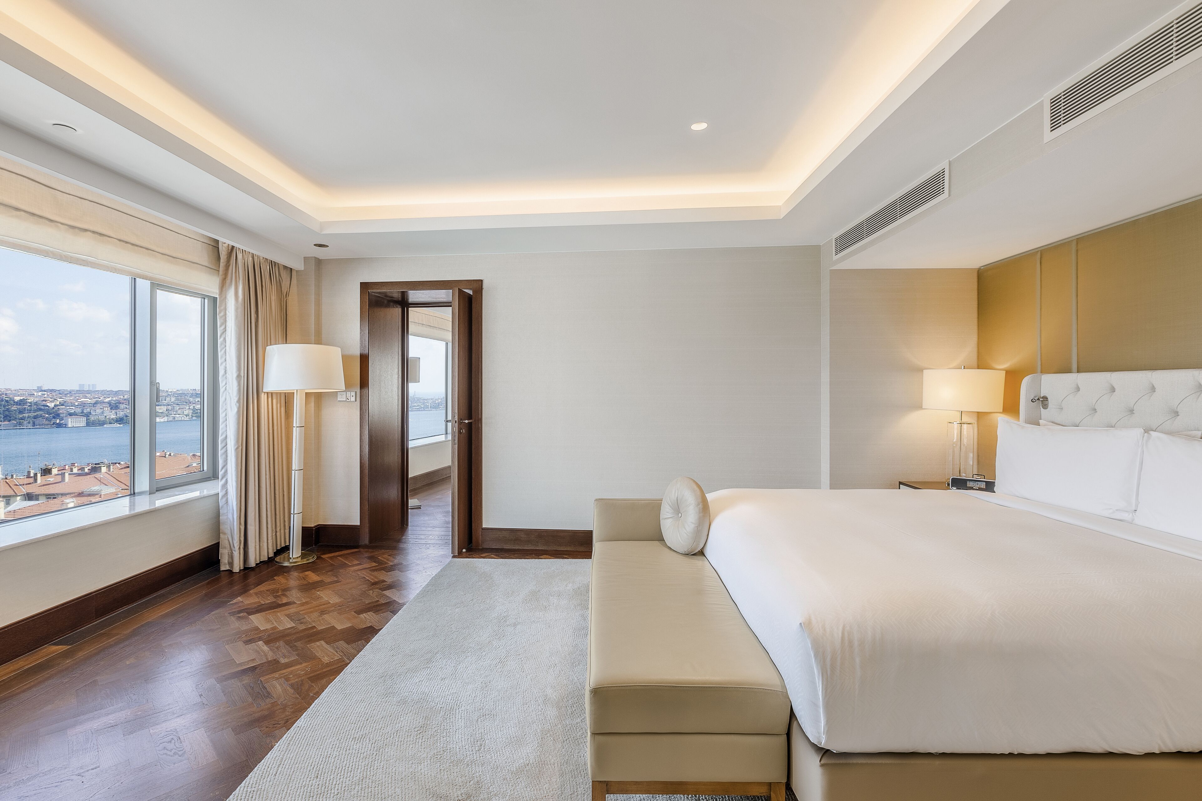 A hotel room with a large bed, a view of the city, and a wooden floor.