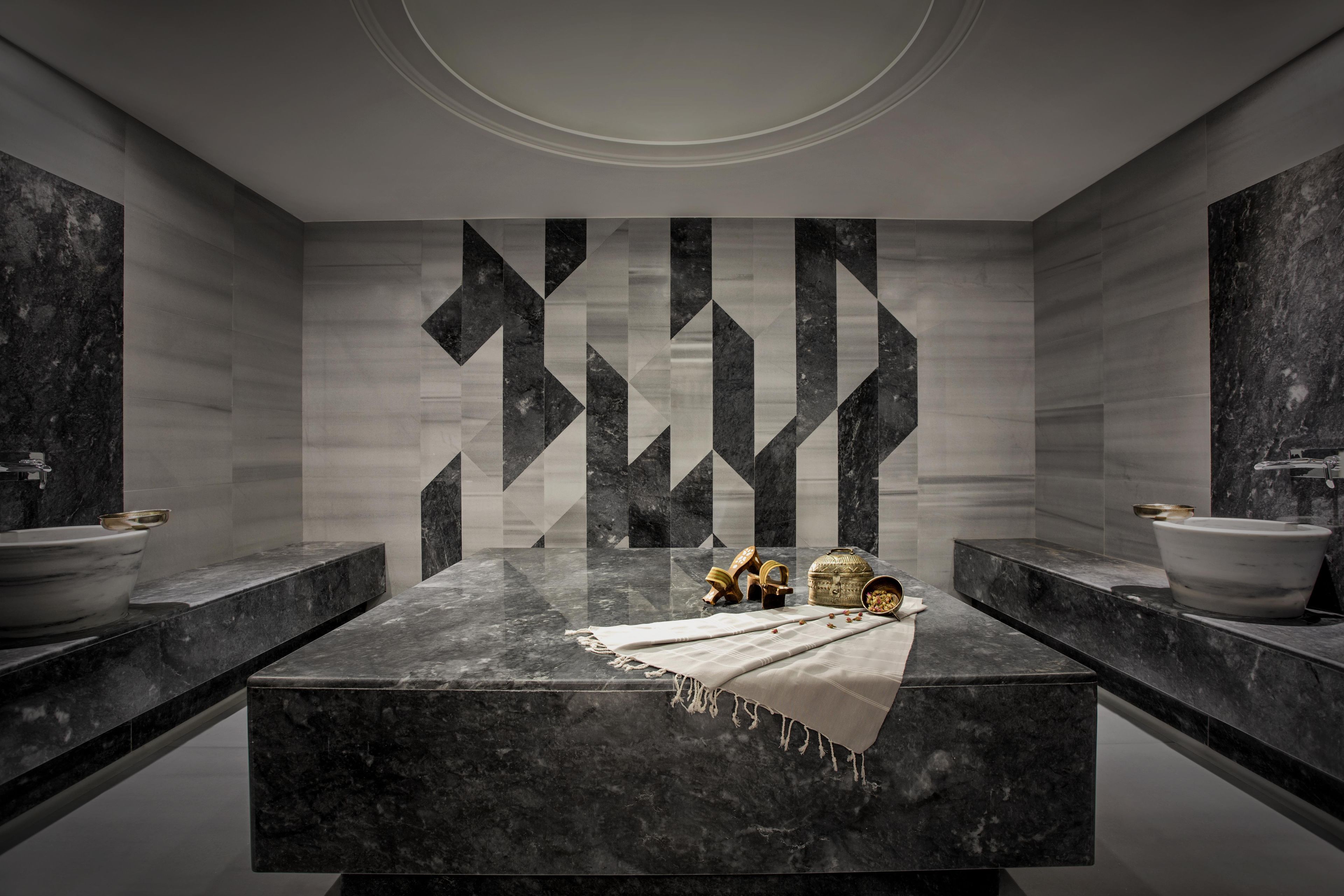 Un baño moderno con un lavamanos de mármol central, dos lavamanos laterales y una pared decorativa con motivos geométricos.