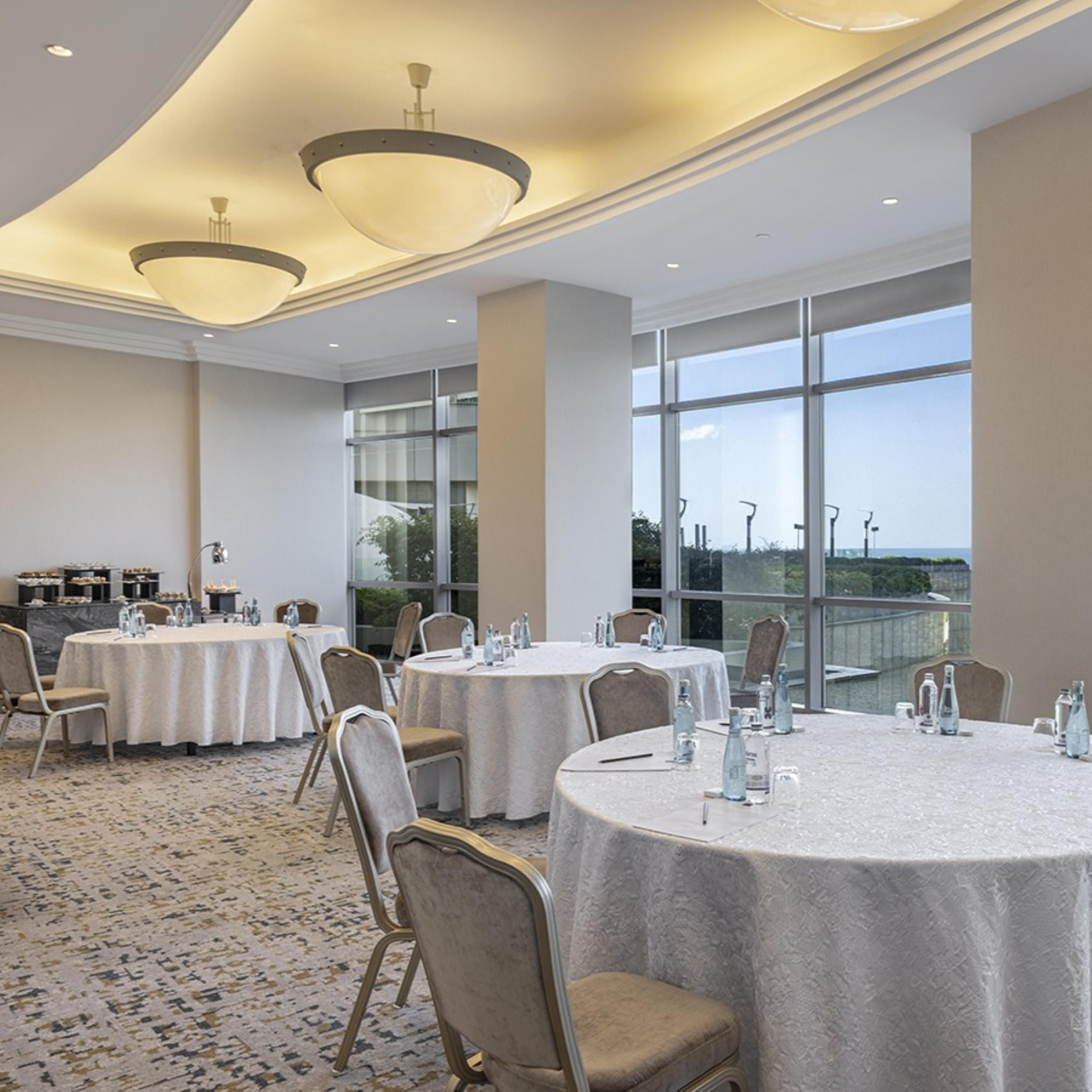 Una sala conferenze con tavoli rotondi, sedie e una grande finestra che offre una vista.