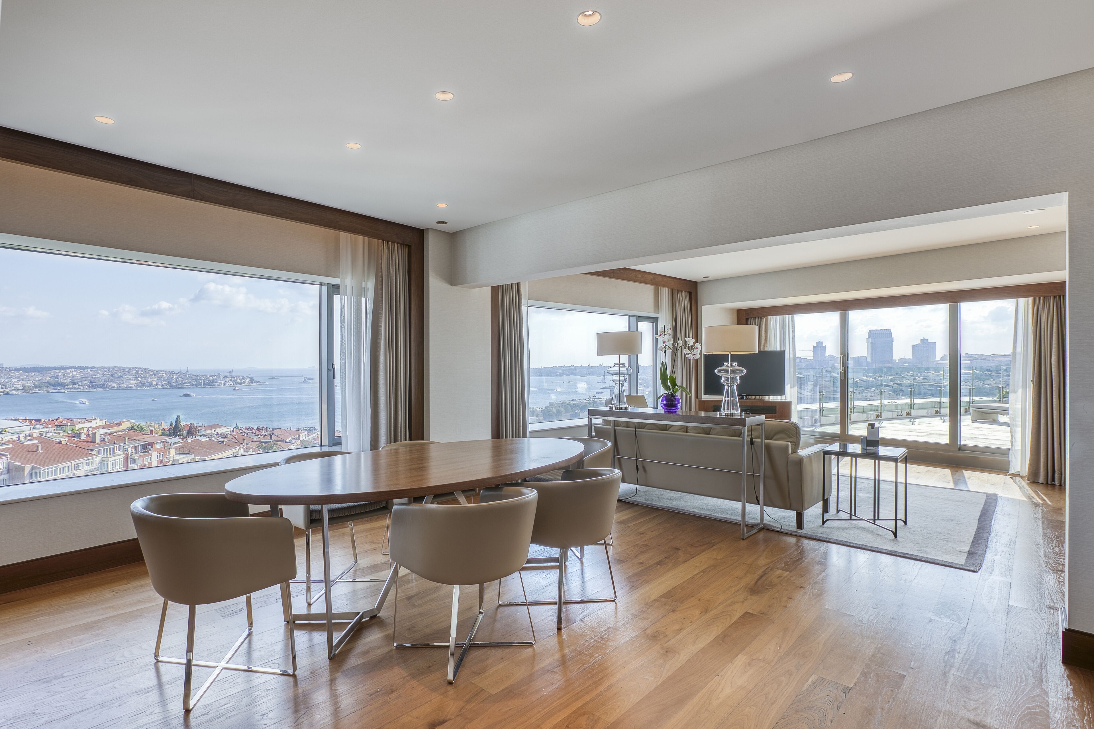Una habitación amplia con una gran mesa de comedor, asientos cómodos, una pequeña cocina y vistas a la ciudad y al agua.