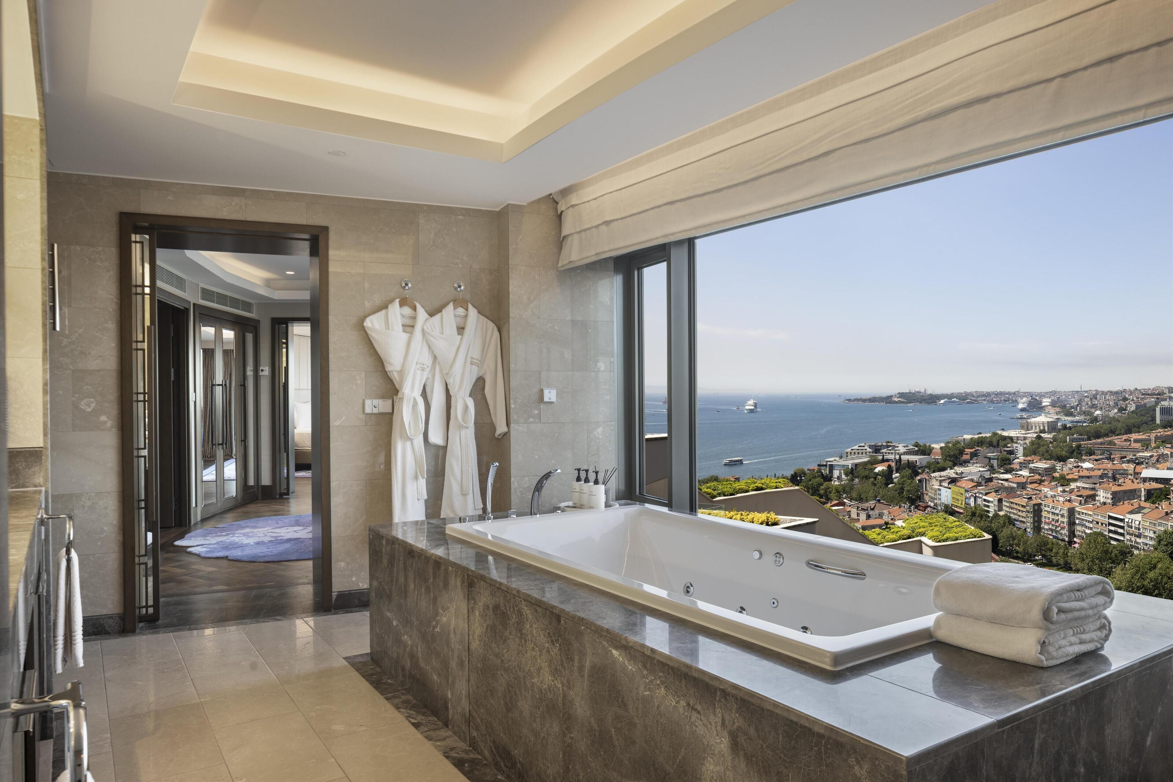 Un baño moderno con una bañera grande, vistas al mar y al paisaje urbano.
