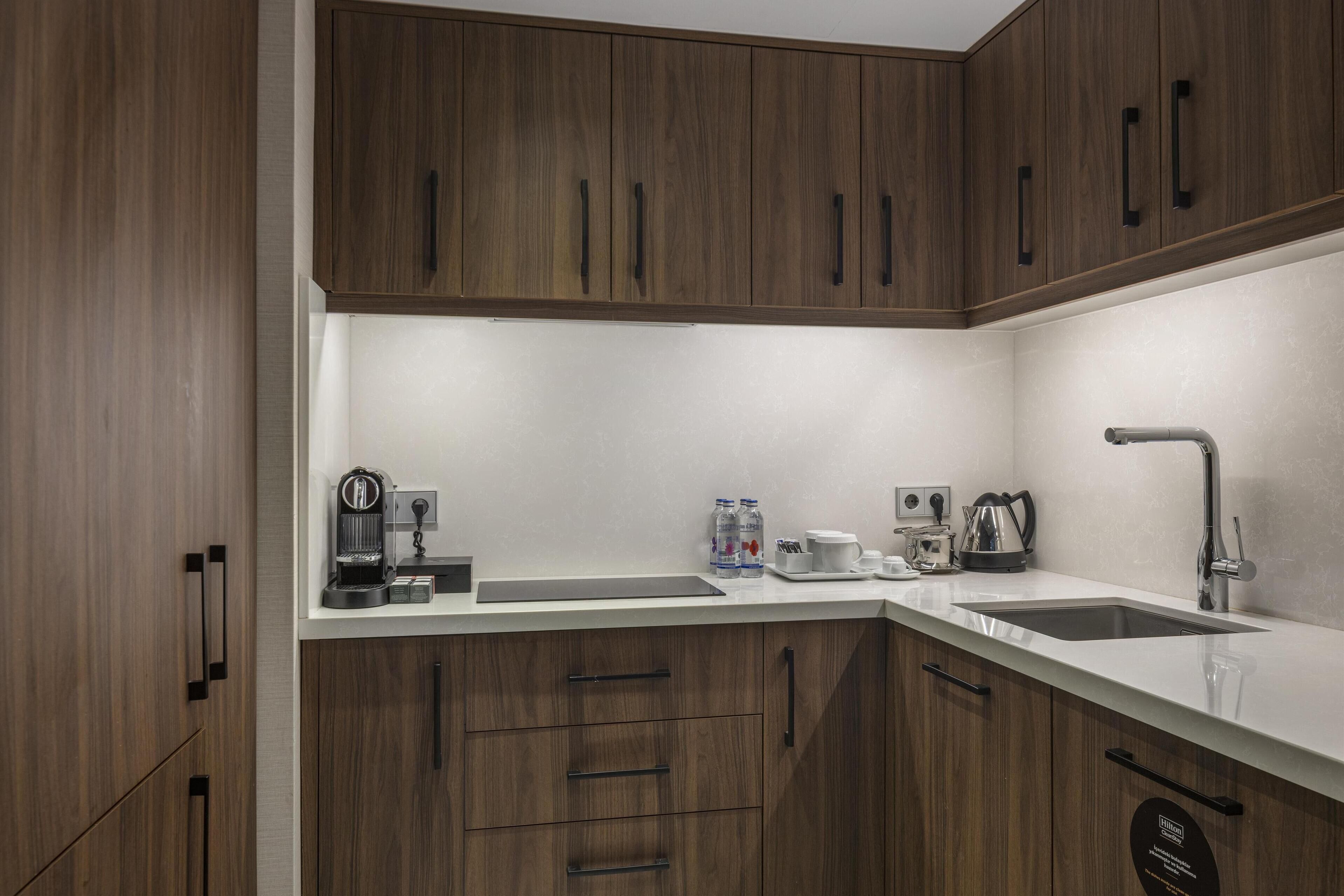 Una cocina moderna con armarios de madera, encimera blanca, cafetera, hervidor y pileta.