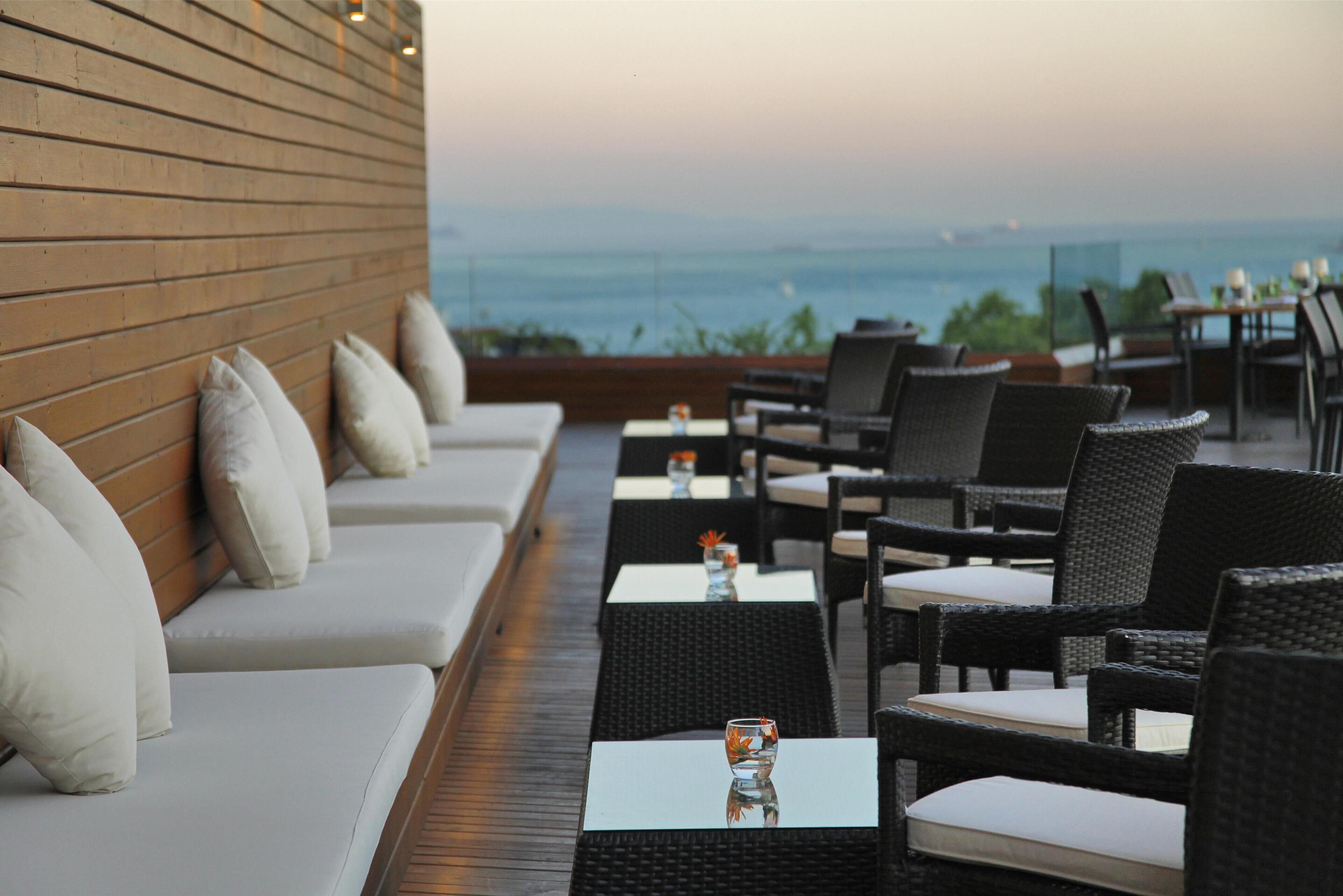 A terrace with outdoor seating, tables, and a view of the sea.