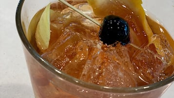 A cocktail with ice cubes, a slice of lemon, and a cherry on a glass.