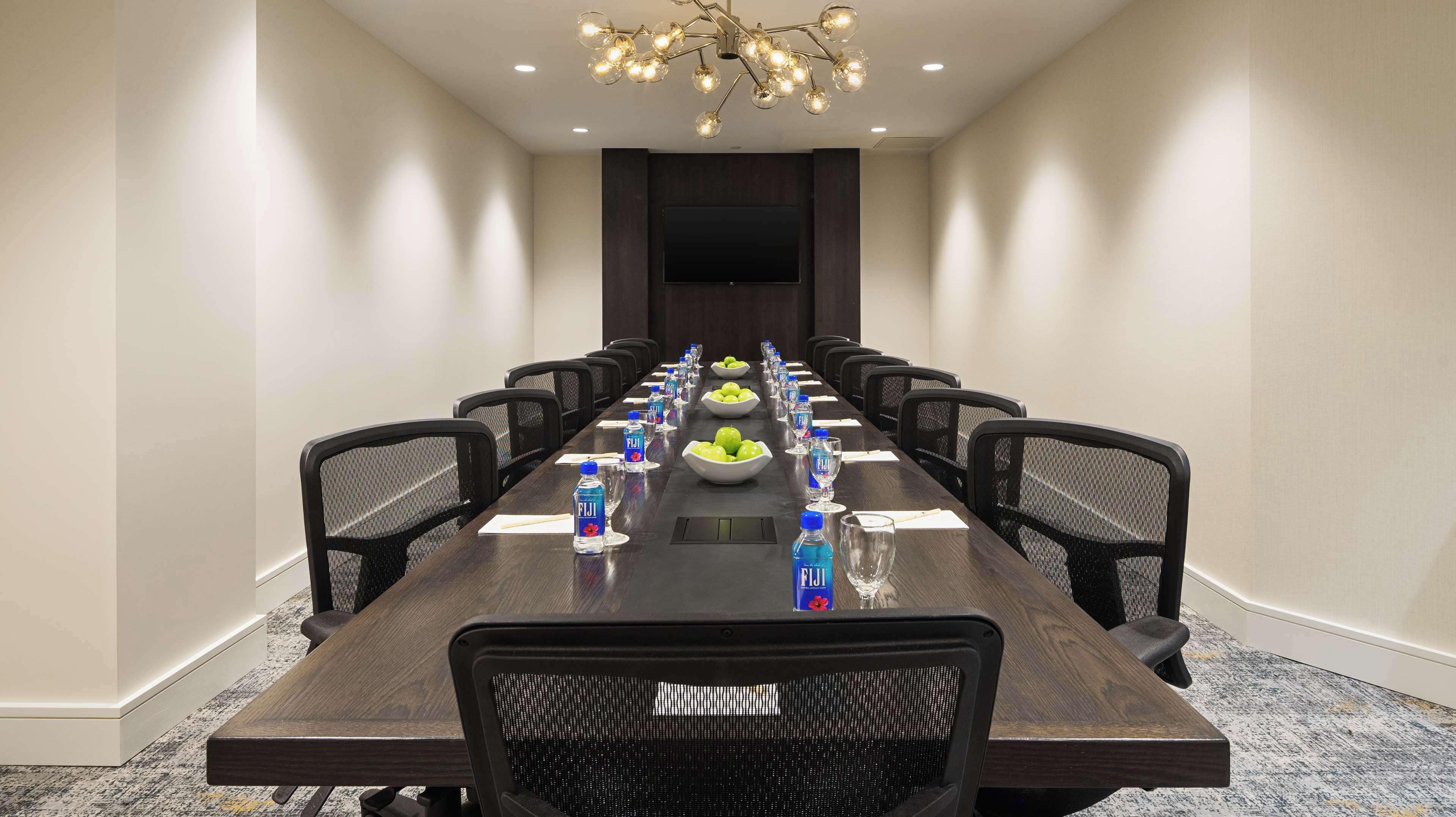 A conference room with a long table, chairs, a large screen, and a chandelier.