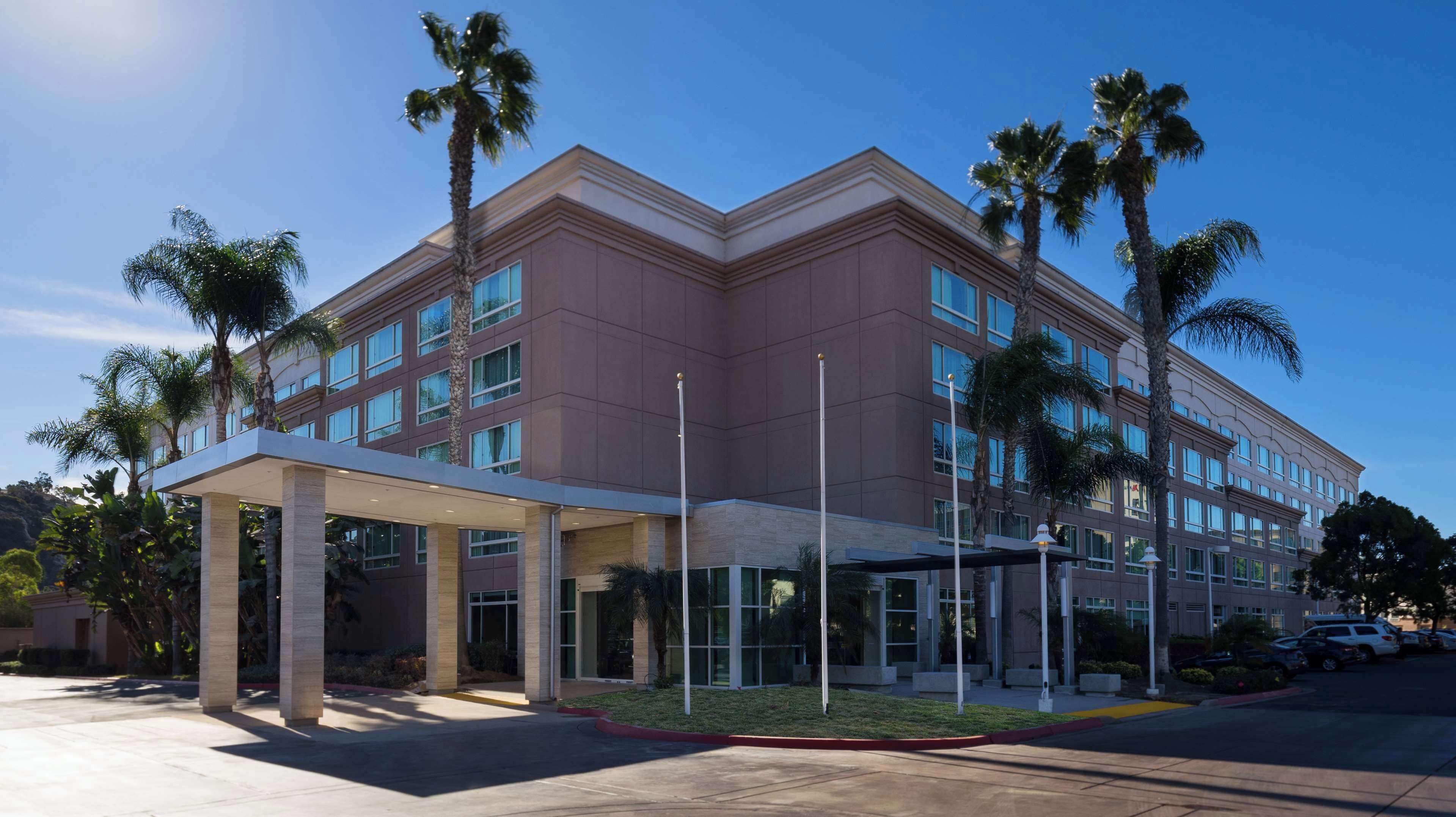 A modern hotel with a covered entrance, multiple floors, and palm trees.