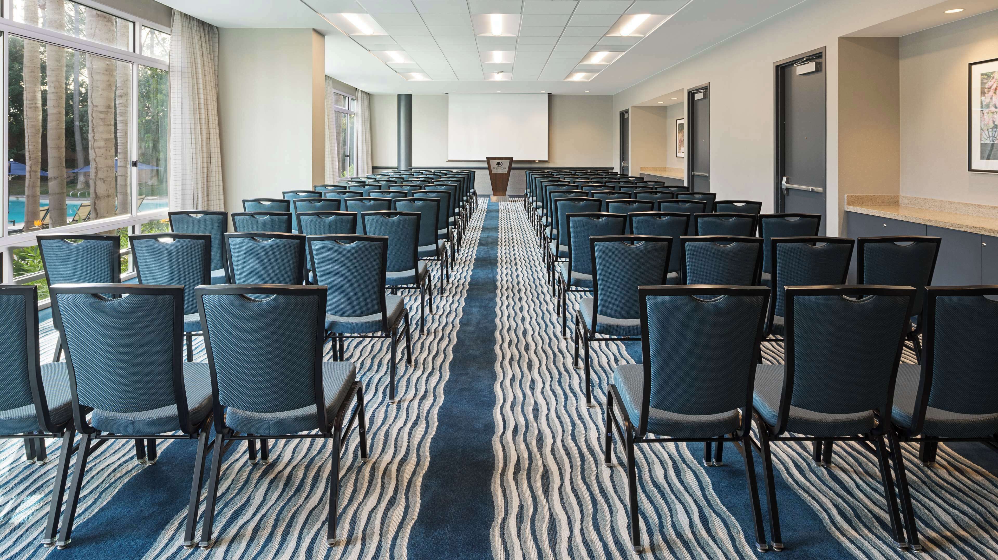 A conference room with rows of chairs, a carpeted floor, and a large screen at the front.