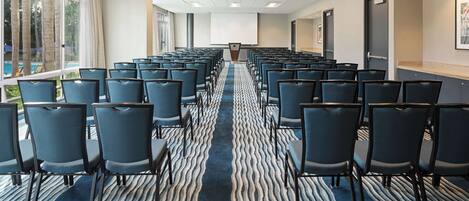 A conference room with rows of chairs, a carpeted floor, and a large screen at the front.
