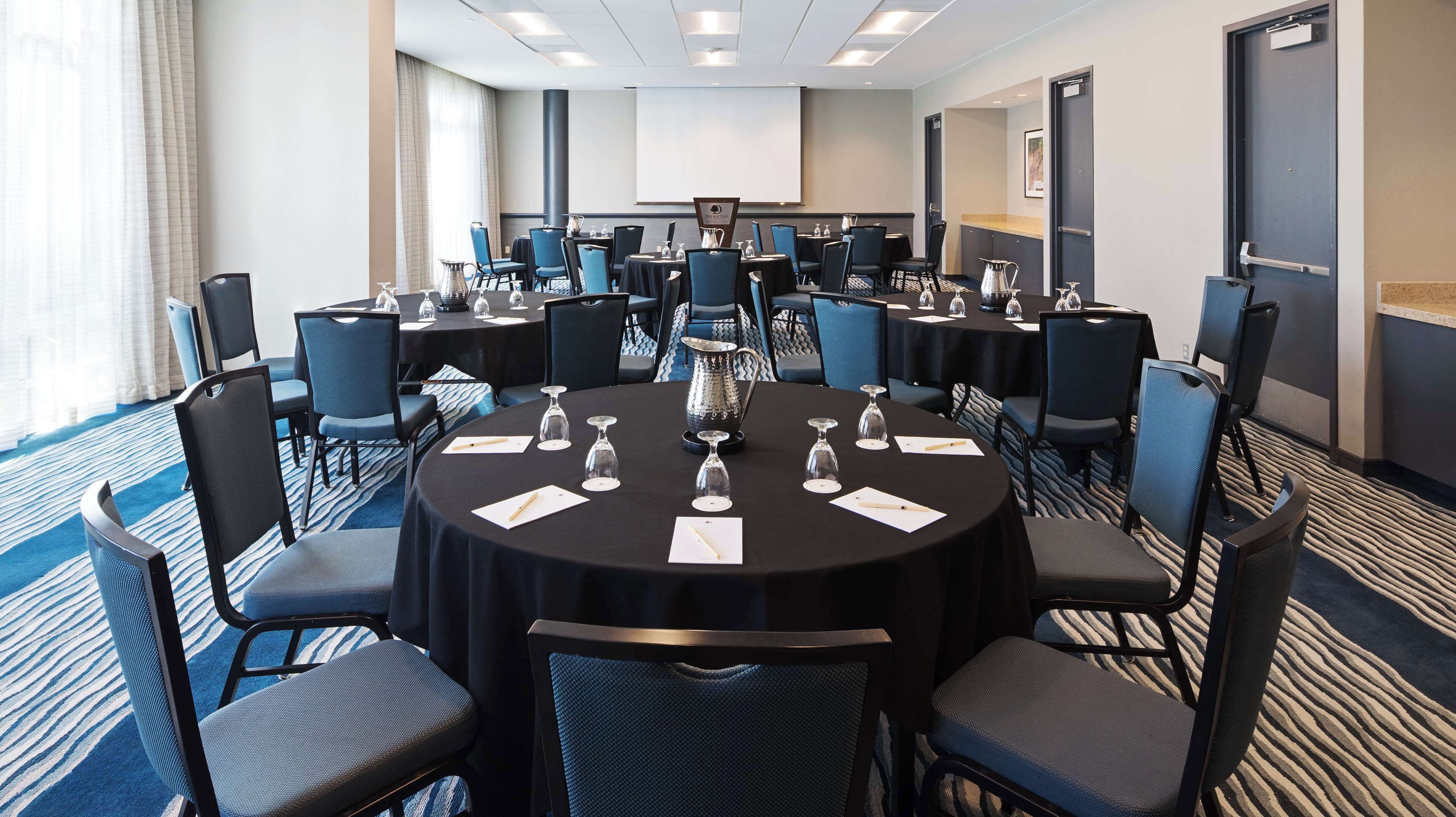 A conference room with multiple tables, chairs, and a large screen.