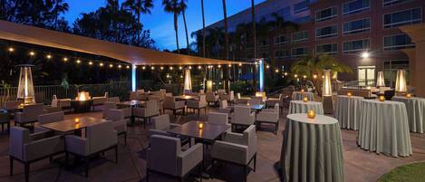An outdoor patio area with tables and chairs, string lights, and a building in the background.