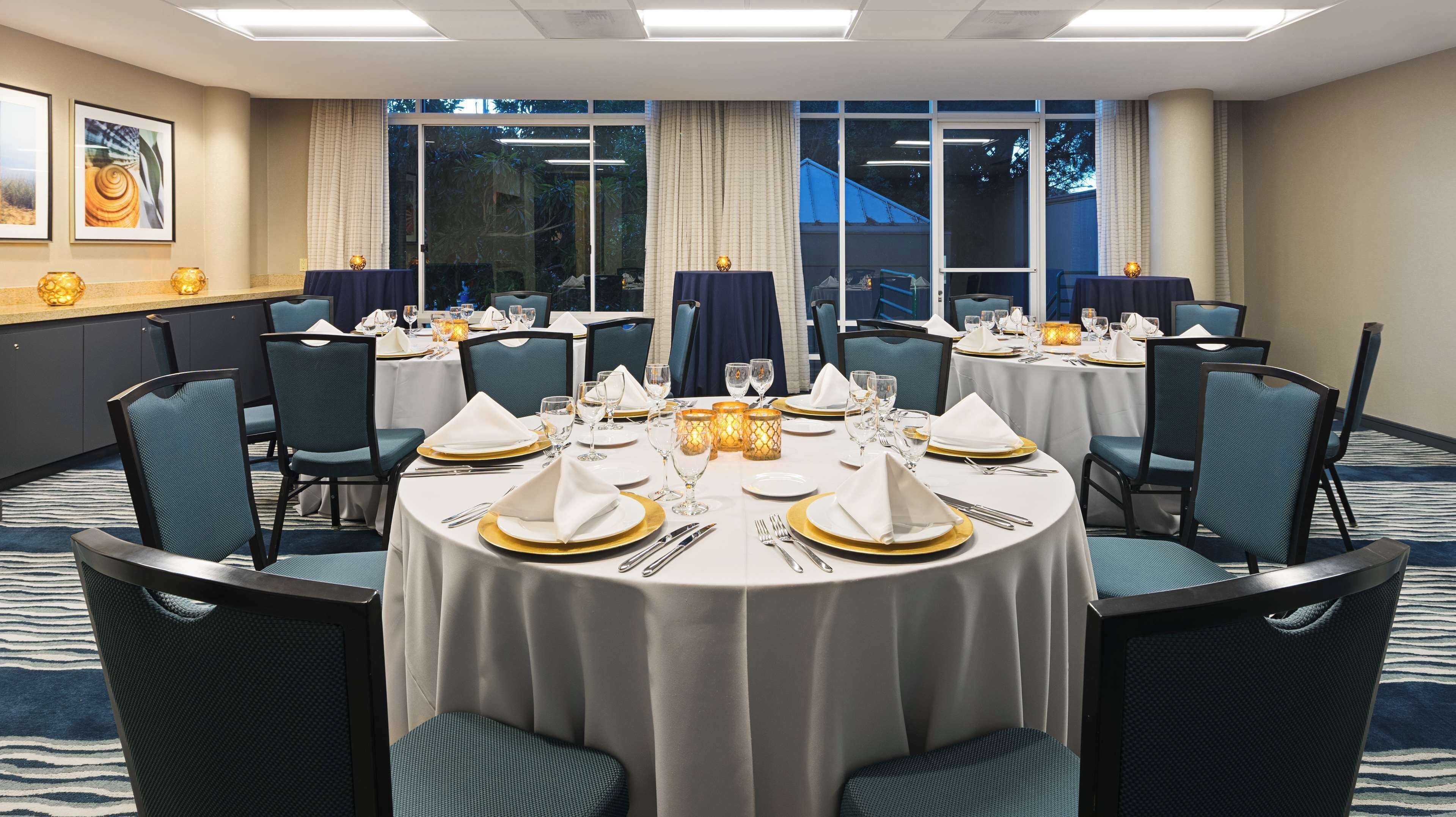 A conference room with round tables, chairs, and a view of the outdoors through large windows.