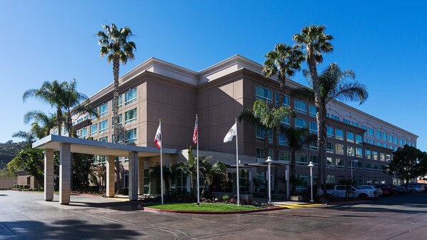 A modern hotel with a two-story structure, a covered entrance, palm trees, and multiple flags. - DoubleTree by Hilton San Diego - Del Mar (San Diego)