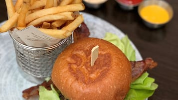 Hamburguesa con tocino, lechuga y pan, acompañada de papas fritas y salsas.