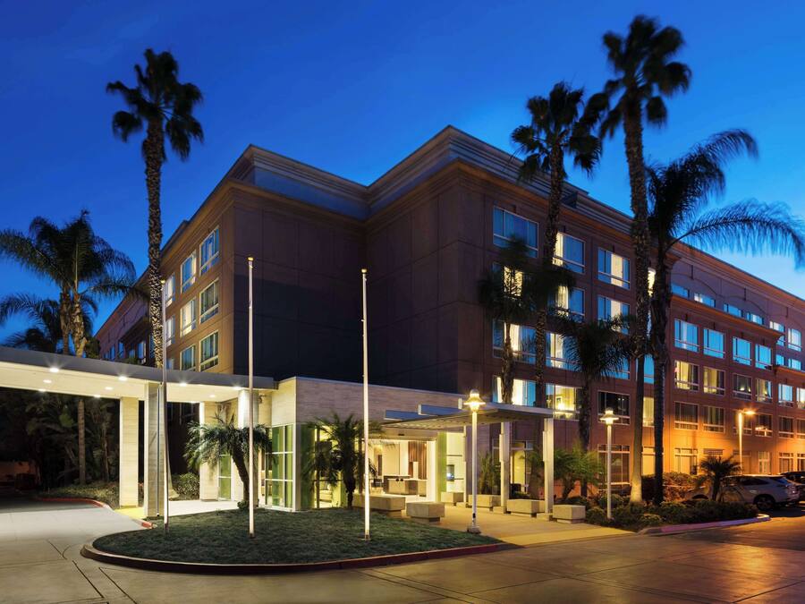 A multi-story hotel with a modern architectural design, featuring a covered entrance area and palm trees.