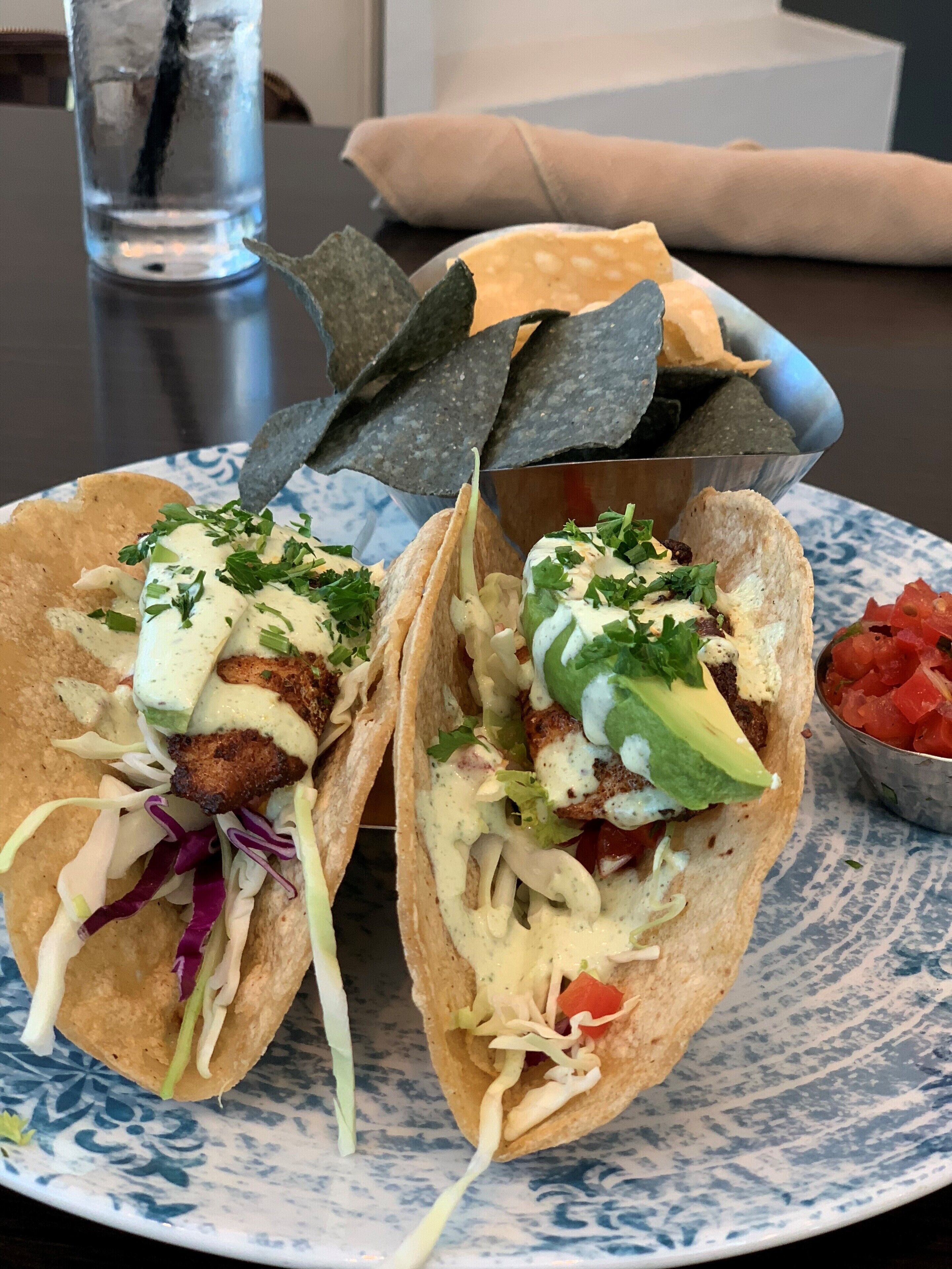 Two tacos with various toppings and a bowl of salsa on a plate.