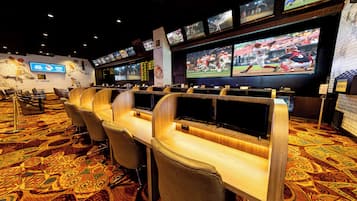 A sports betting area with multiple screens, a brick wall with a large screen, and a carpeted floor.