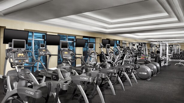 Una palestra con diverse macchine per esercizi, tra cui tapis roulant ed ellittiche, disposte in file.