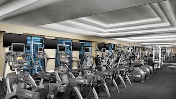 Un gimnasio con varias máquinas de ejercicio, incluyendo cintas de correr y elípticas, dispuestas en filas.