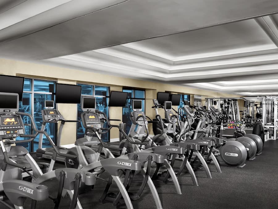 A gym with multiple exercise machines, including treadmills and elliptical trainers, arranged in rows.