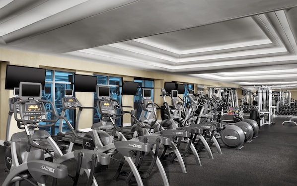 Une salle de sport équipée de nombreux appareils d’exercice, notamment des tapis de course et des vélos elliptiques, disposés en rangées.