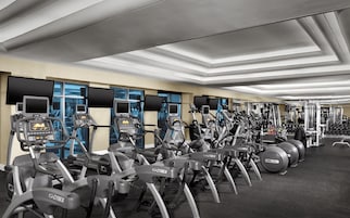 Un gimnasio con varias máquinas de ejercicio, incluyendo cintas de correr y elípticas, dispuestas en filas.