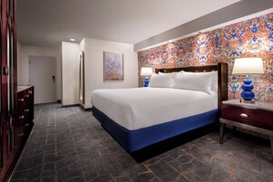 Una habitación de hotel con una cama grande, dos mesitas de noche, una lámpara de pared y una puerta.