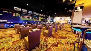 Un casino con varias pantallas mostrando eventos deportivos, filas de asientos acolchados y una alfombra estampada.