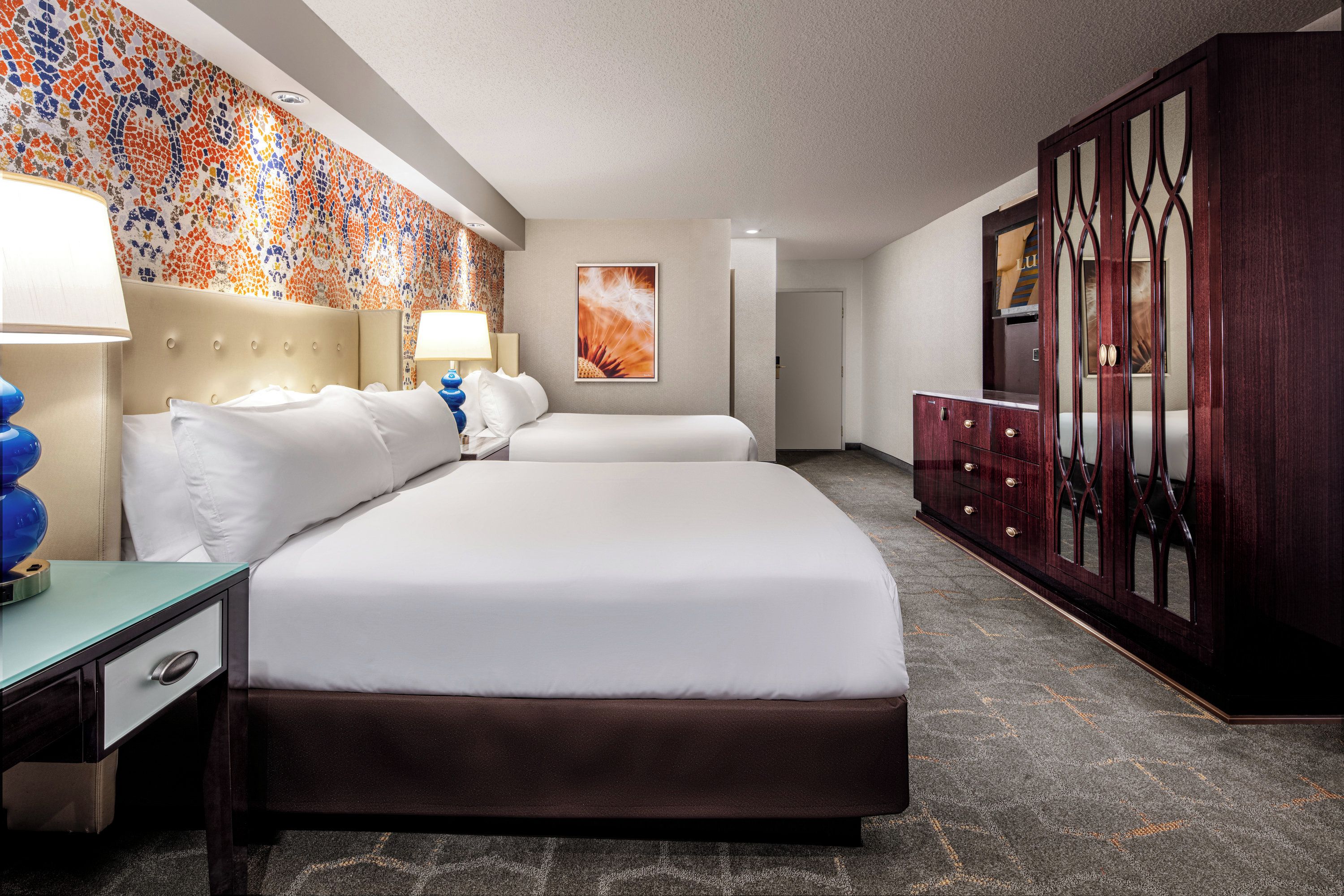 A hotel room with a large bed, two bedside tables, a wardrobe, and a colorful mosaic wall.