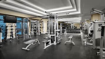 Un gimnasio con diversos equipos de ejercicio, estantes para pesas y bancos.