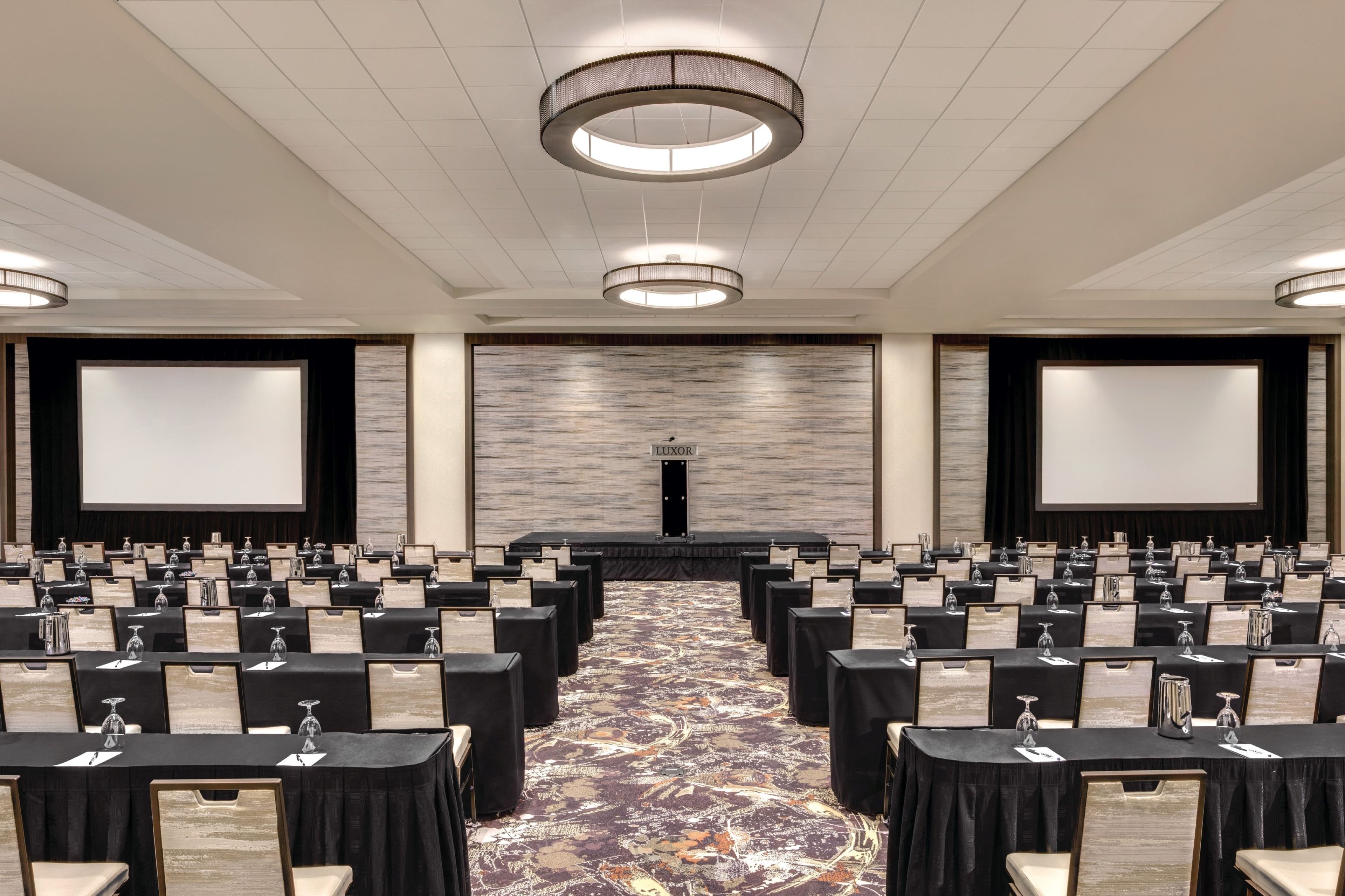 A conference room with rows of tables, a stage, and a large screen.
