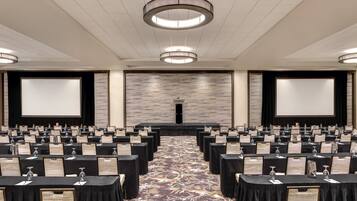 A conference room with rows of tables, a stage, and a large screen.