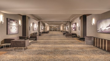 Un pasillo de hotel con piso alfombrado, zonas de estar y obras de arte en las paredes.