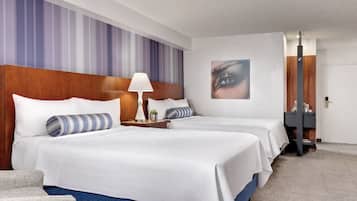 Habitación de hotel con dos camas, una mesita de noche con lámpara, un cuadro colgado en la pared y una puerta con espejo.