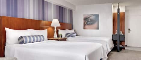 Habitación de hotel con dos camas, una mesita de noche con lámpara, un cuadro colgado en la pared y una puerta con espejo.