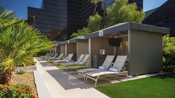 A row of outdoor lounge chairs with a poolside view, a small kiosk, and a building in the background.