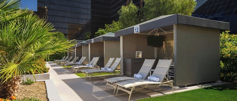 Una fila de sillones de exterior con vista a la piscina, un pequeño quiosco y un edificio al fondo.