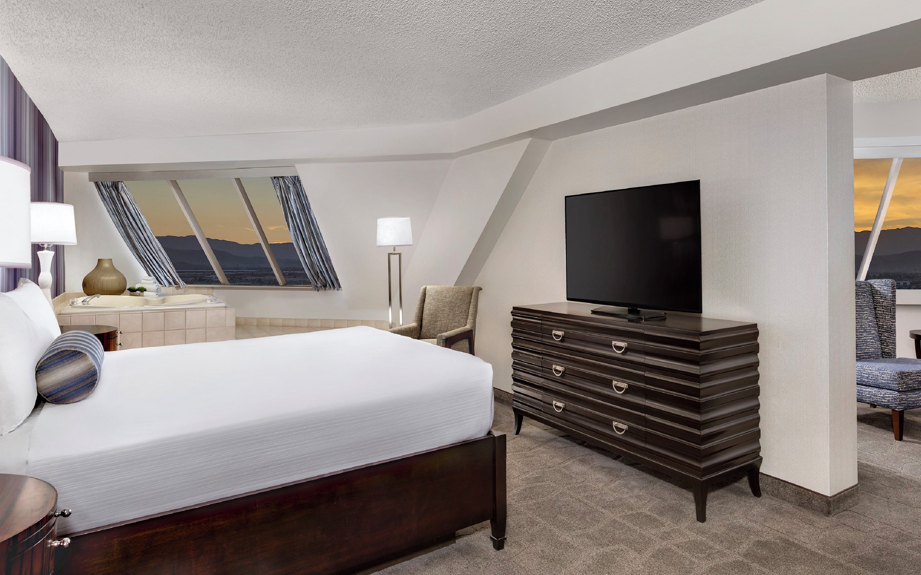 A hotel room with a bed, a dresser, a flat-screen TV, a chair, and a large window with a view.