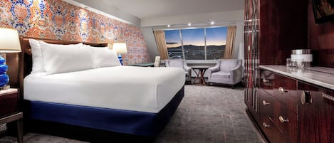 A hotel room with a large bed, a desk, a chair, a wardrobe, and a view of the cityscape.