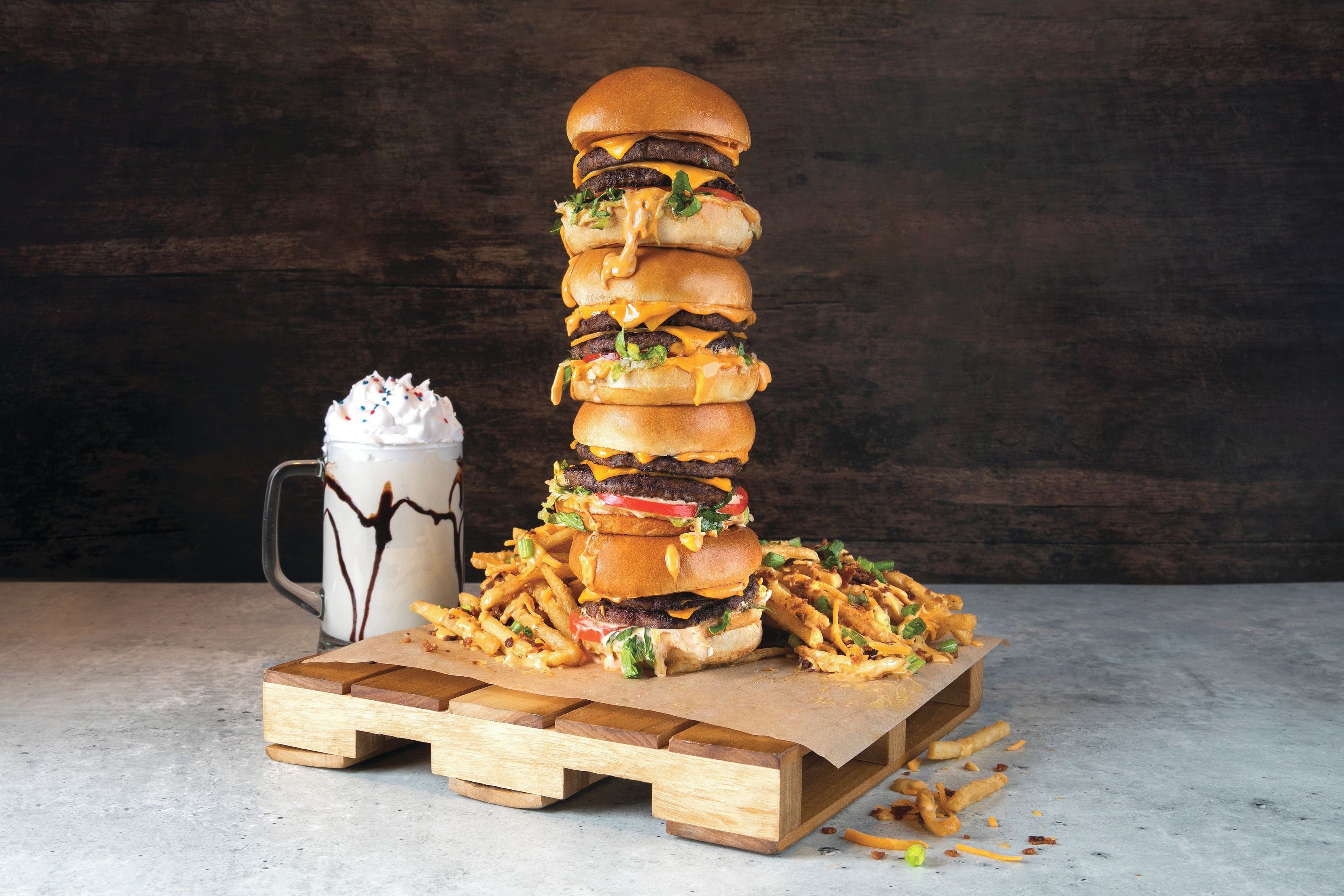 Una alta pila de hamburguesas, papas fritas y un batido sobre una tabla de madera.