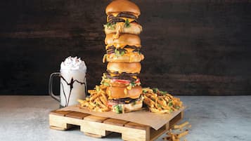 Una alta pila de hamburguesas, papas fritas y un batido sobre una tabla de madera.