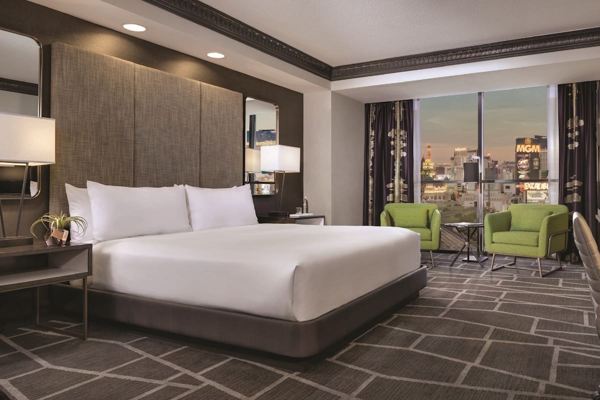 Une chambre d’hôtel avec un grand lit, un bureau avec une télévision, une chaise et une vue sur le paysage urbain.